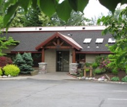 Exterior of the dental office building featuring a wooden gabled entrance, stone pillars, and lush green landscaping under a clear sky